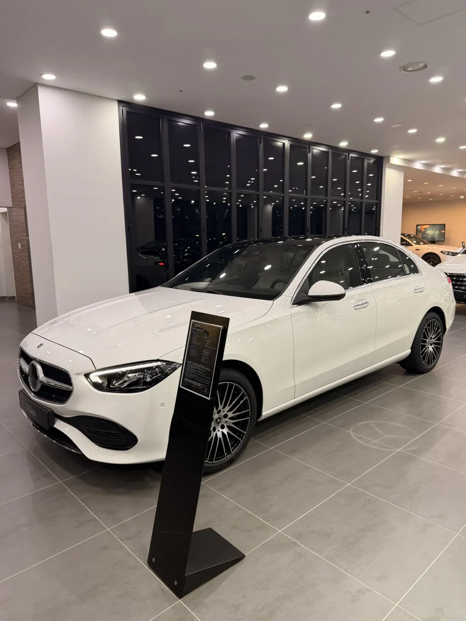 안내 스탠드 옆에 전시된 흰색 벤츠 C-Class 세단