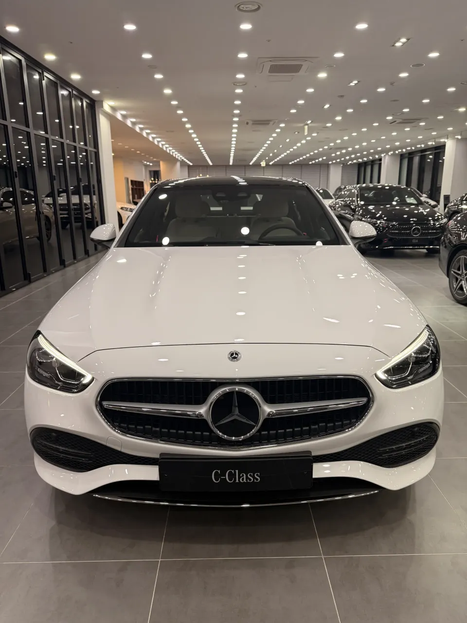 쇼룸에 전시된 흰색 벤츠 C-Class 세단 정면